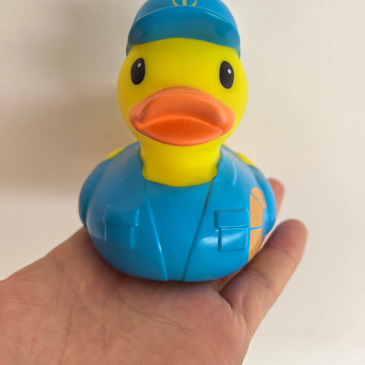 A yellow rubber duck bath toy with an orange beak and blue body is held in a hand.