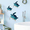 A collection of teal and green whale wall art sculptures displayed on a light blue wall above a white sink.