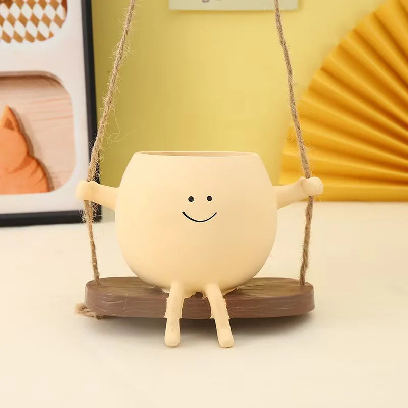 A light beige resin ornament shaped like a smiling face is hanging by twine against a yellow background.