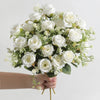 A hand holds a bouquet of white silk touch artificial roses for home and event decor.