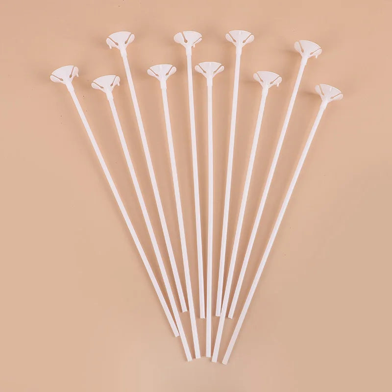 A collection of white macaron balloon sticks with holder cups arranged diagonally on a beige background.
