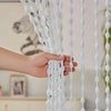 A hand is touching a white beaded string curtain with tassels used as a bohemian door and window drape.