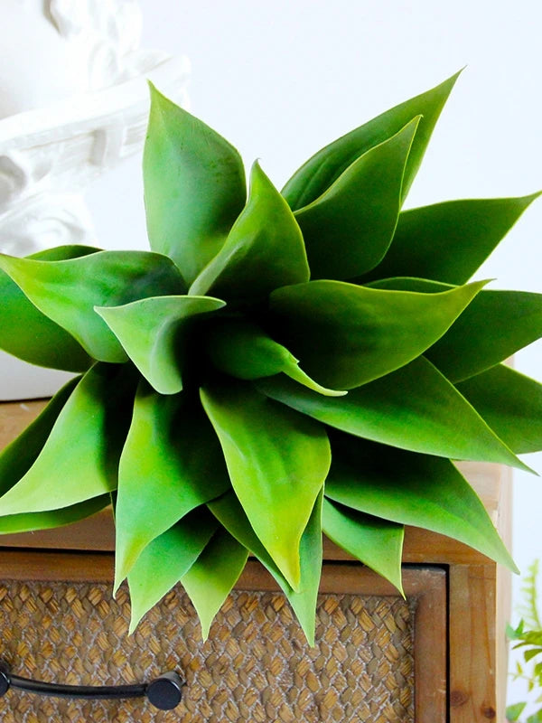 A vibrant green artificial agave plant with thick, fleshy leaves displayed on a wooden surface.