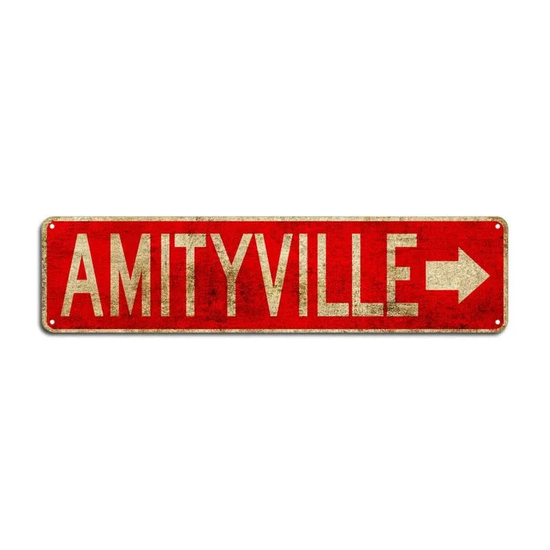 A rustic red metal sign with gold lettering spelling out AMITYVILLE and an arrow.