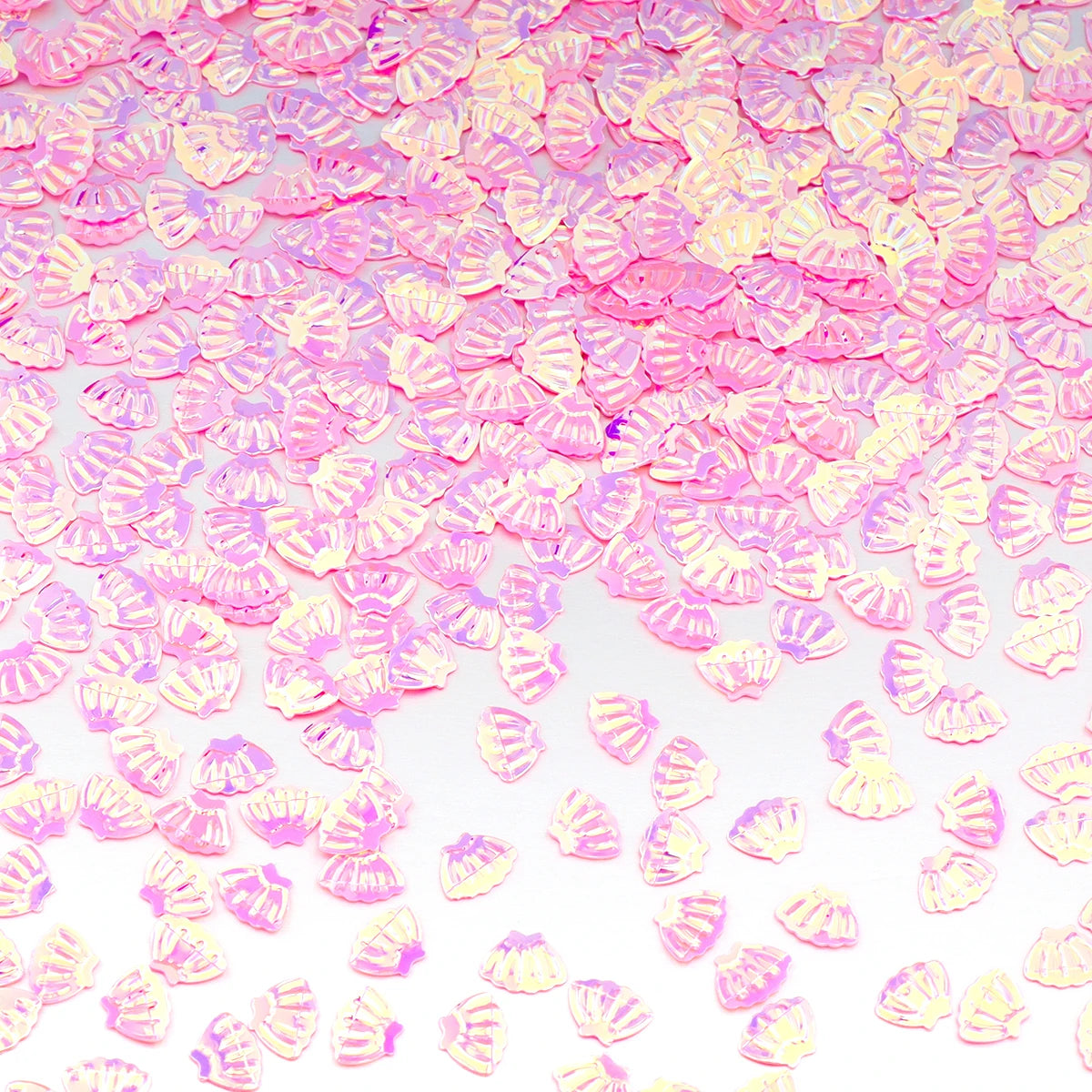 Pink and yellow sea shell PVC sequins scattered on a white background for nail art and craft decoration