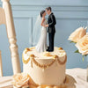 A wedding cake featuring an elegant bride and groom topper, surrounded by roses and gold accents.
