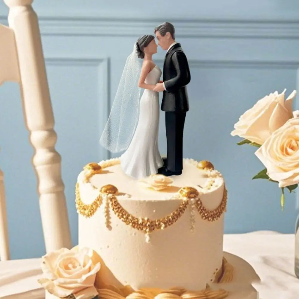 A wedding cake featuring an elegant bride and groom topper, surrounded by roses and gold accents.
