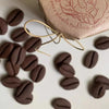 A brown coffee bean stamp mold is shown with loose beans on a white surface.