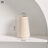 A tall, beige ceramic vase with a textured finish is displayed on a white shelf.