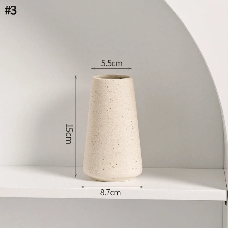 A tall, beige ceramic vase with a textured finish is displayed on a white shelf.