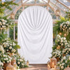 A white fabric drape covers an archway decorated with lush floral arrangements and hanging lanterns for a wedding or event ba