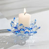 A clear crystal lotus candle holder with a white candle and flame on a white marble surface.