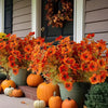 Bouquet de fleurs d'automne artificielles orange et jaune devant une porte sombre.