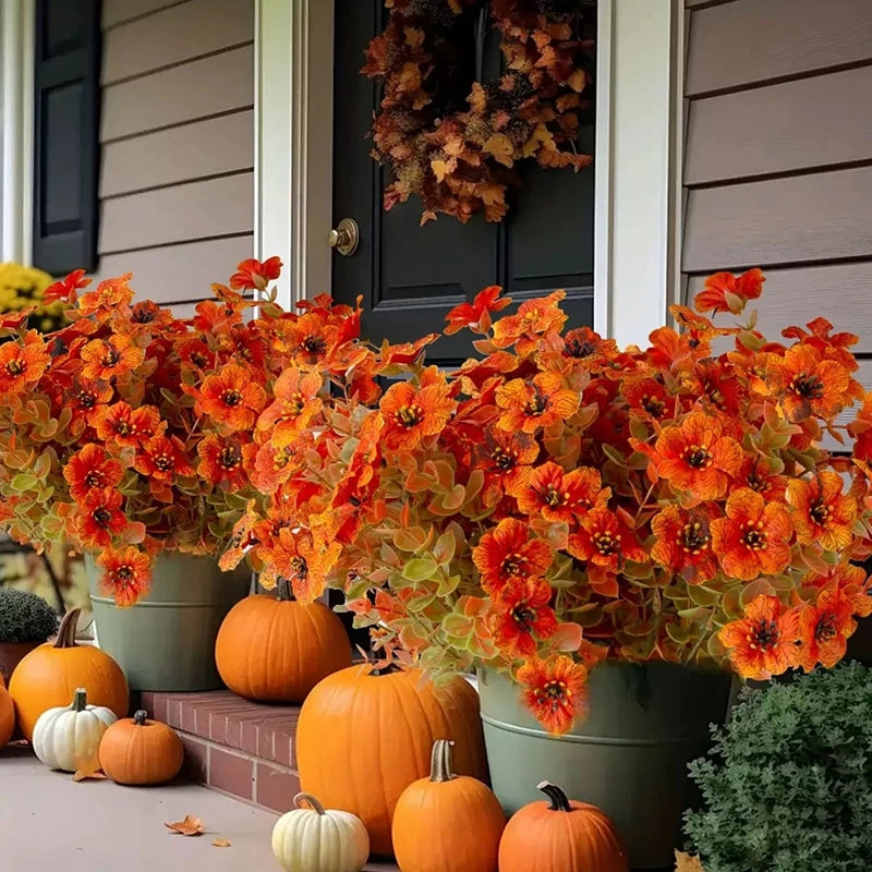 Bouquet de fleurs d'automne artificielles orange et jaune devant une porte sombre.