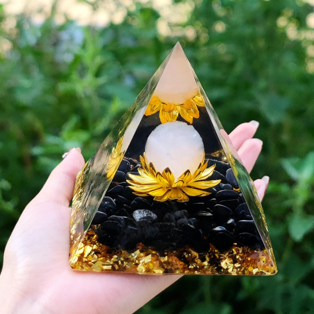Hand holding a clear resin pyramid with natural obsidian and a golden copper coil inside