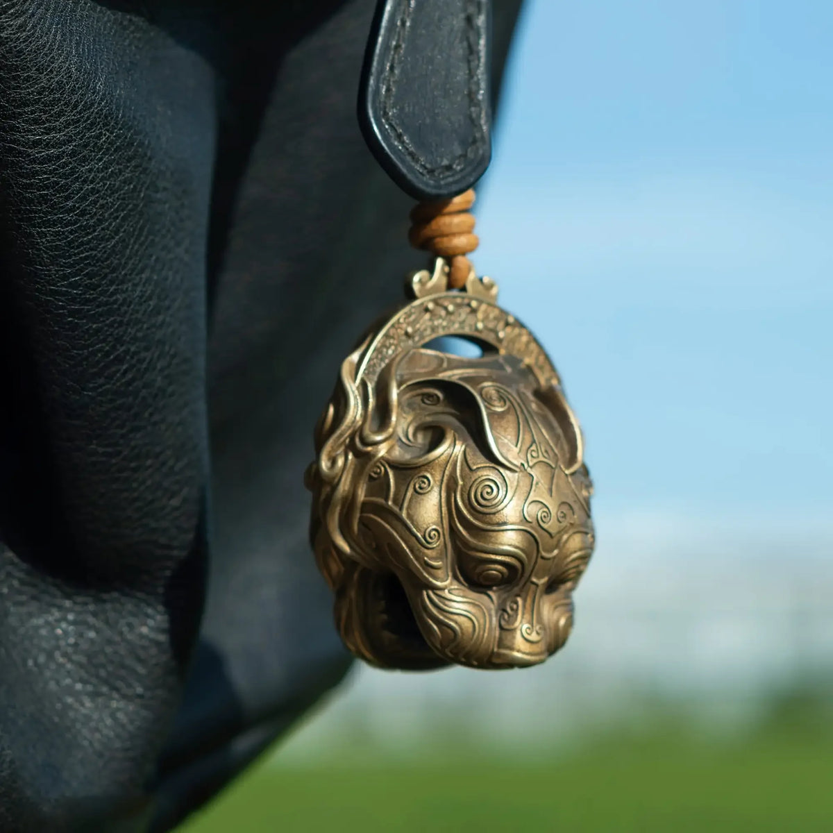 A pure copper lucky tiger head bell with intricate swirling design hanging from a leather strap.