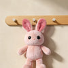 Pink fluffy rabbit plush toy hanging from a wooden wall hook rack.