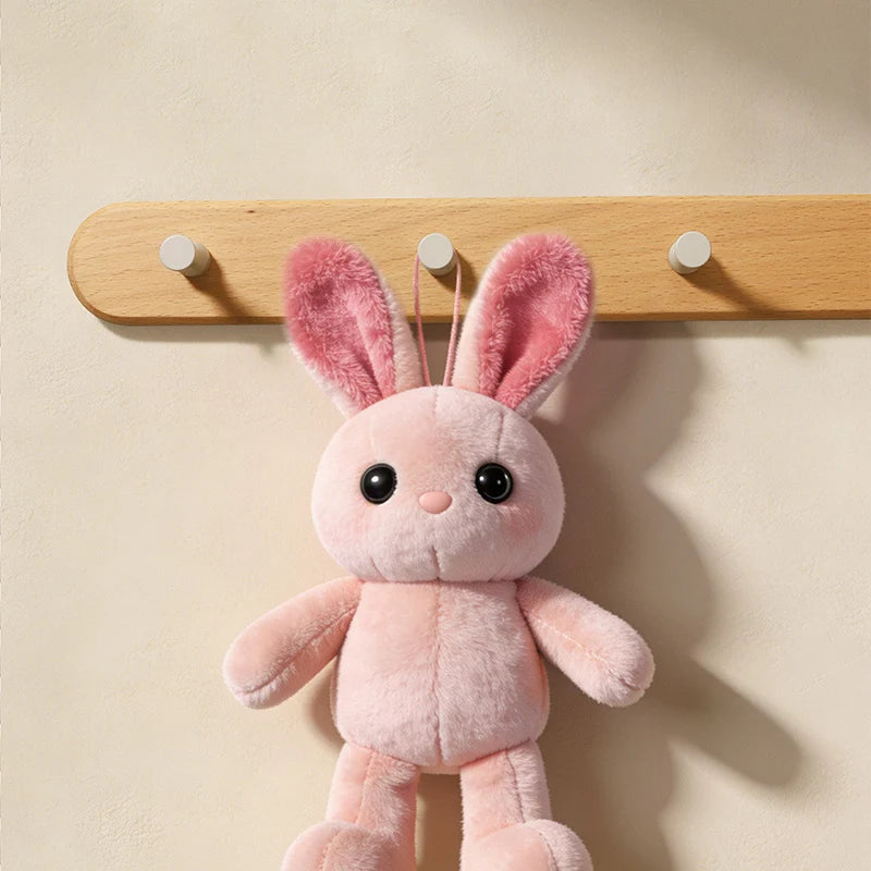 Pink fluffy rabbit plush toy hanging from a wooden wall hook rack.