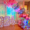 A colorful balloon arch decoration featuring pink, purple, and blue balloons with a sparkly silver backdrop.