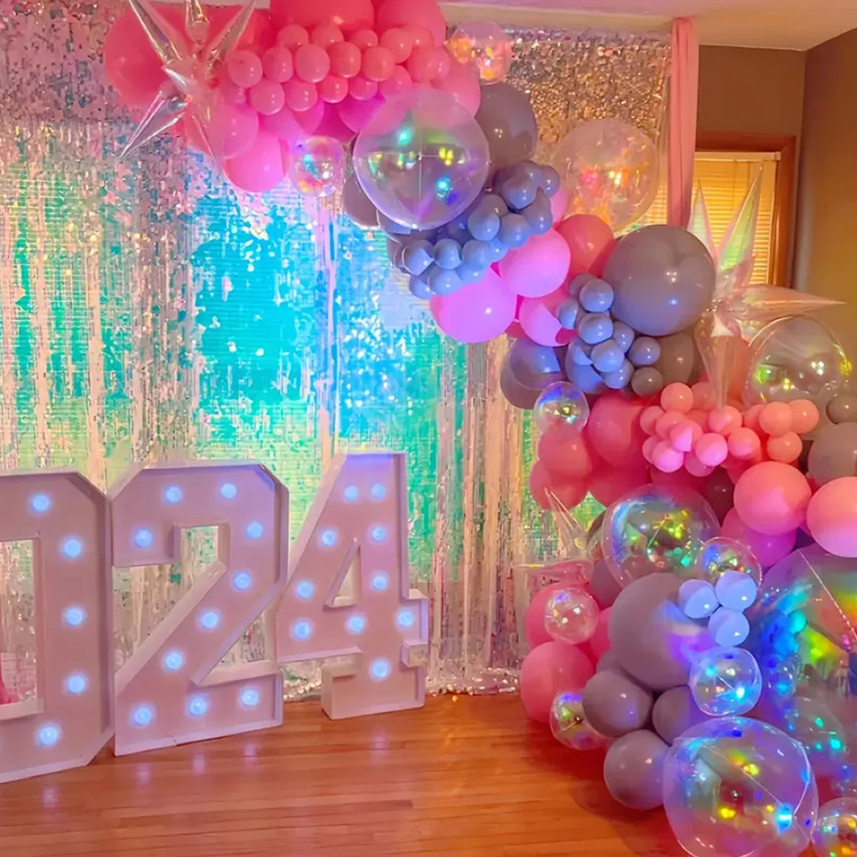 A colorful balloon arch decoration featuring pink, purple, and blue balloons with a sparkly silver backdrop.