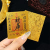 A hand holds two gold-colored rectangular stickers with Chinese characters on a black background.