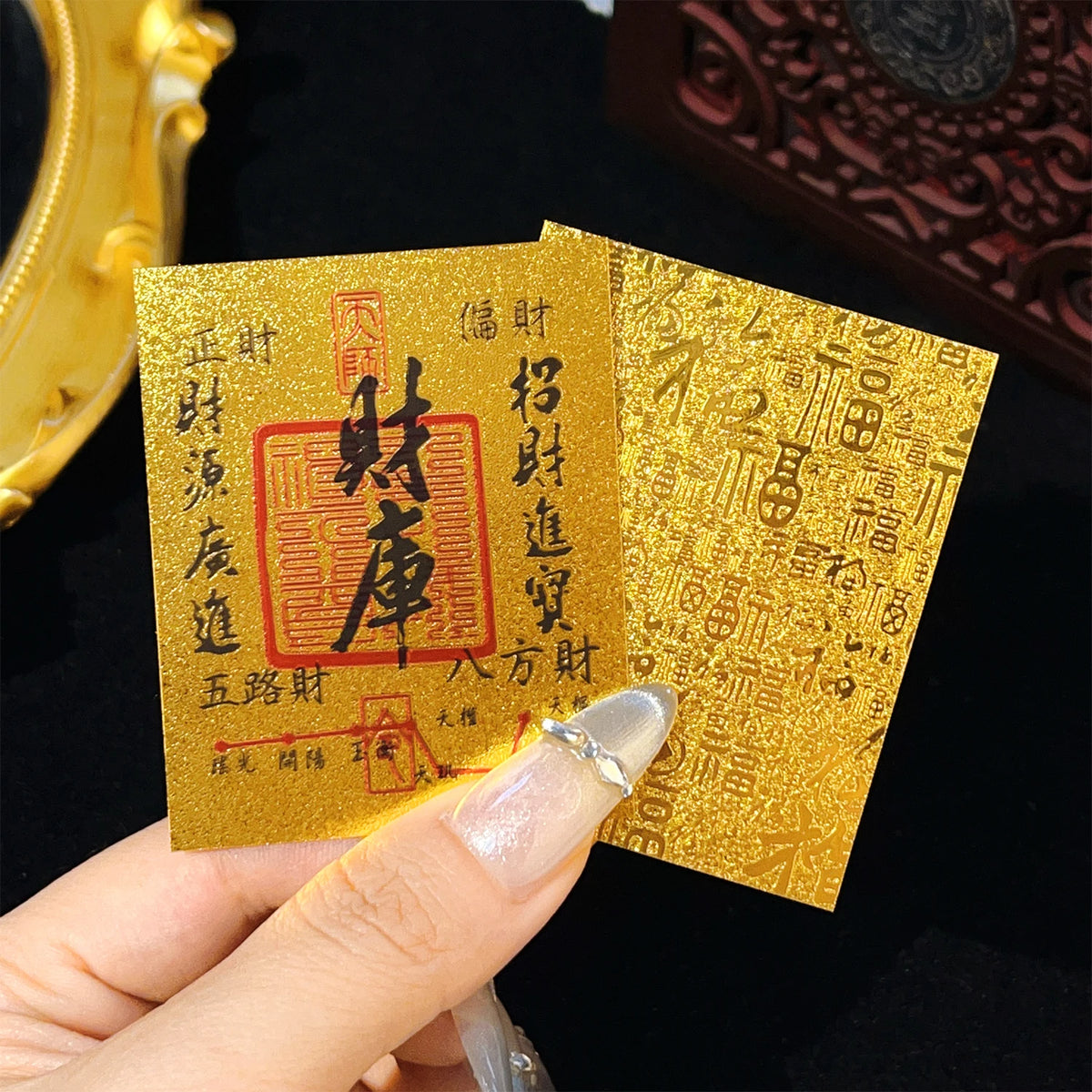 A hand holds two gold-colored rectangular stickers with Chinese characters on a black background.