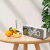 A white LED digital alarm clock displaying 12:30 on a wooden table next to an orange and lemon.
