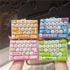 A hand holds a colorful keyboard keycap keychain featuring various cartoon animal designs and colors.