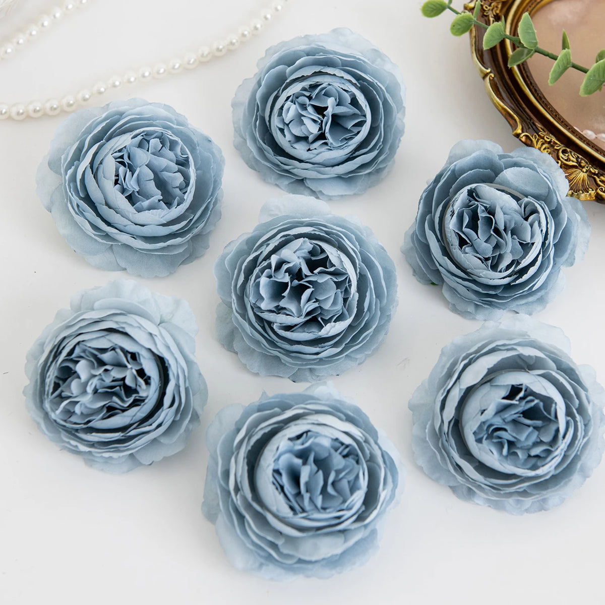 A collection of light blue silk peony artificial flowers arranged on a white surface.