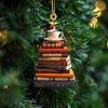 Ornement acrylique doré en forme de livres empilés surmontés d'une tasse de thé, suspendu à une branche d'arbre de Noël vert.