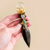 A hand holds a decorative crystal ball featuring amethyst and obsidian stones set in gold-toned metalwork on a dark wood piec