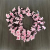 A circular wreath made of pink artificial flowers strung on an LED rattan light wire for seasonal decoration.
