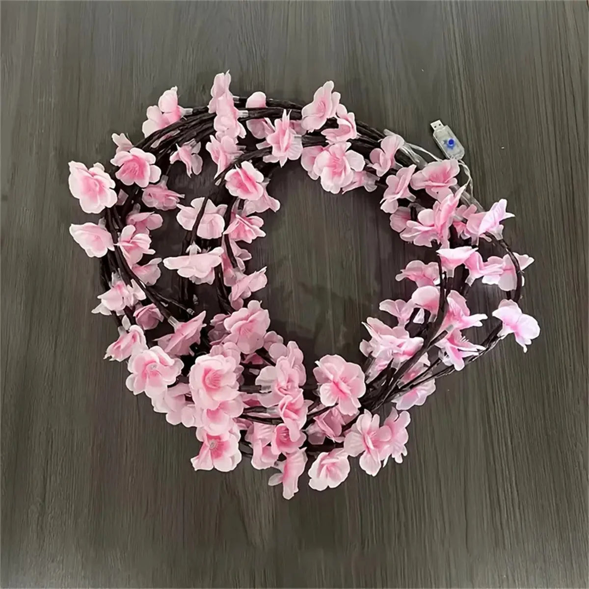 A circular wreath made of pink artificial flowers strung on an LED rattan light wire for seasonal decoration.