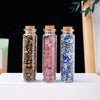 Three glass bottles filled with natural crystals: brown, pink, and blue, standing on a white surface.