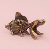 A retro brass goldfish statue with textured scales and fins, displayed against a light pink background.