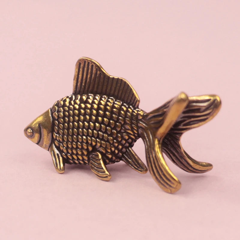 A retro brass goldfish statue with textured scales and fins, displayed against a light pink background.