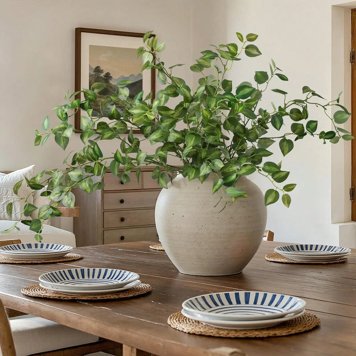 A large potted artificial eucalyptus stem with silk green leaves sits on a wooden table.