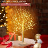 A decorative LED birch tree with warm yellow lights stands on a wooden surface.
