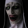 A close-up of a white latex mask resembling a grotesque, aged face with glowing green eyes and bared teeth.