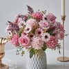A bouquet of artificial silk pink and purple flowers arranged in a white vase on a table.