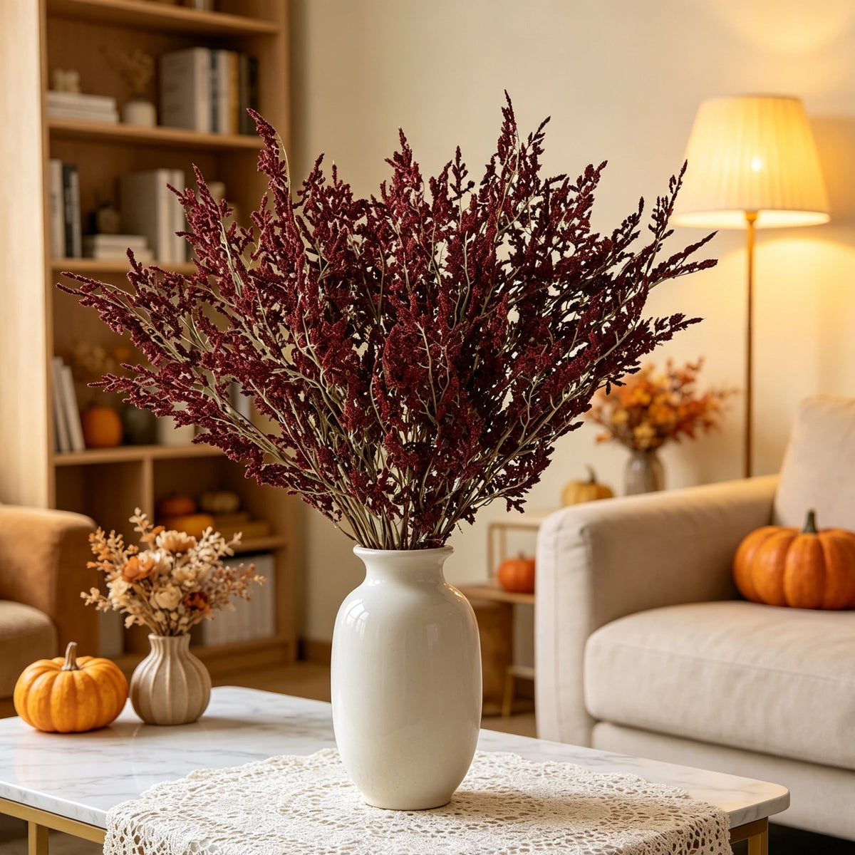 A vase filled with deep red artificial silk lover grass on a white table in a bright living room setting.