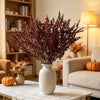 A vase filled with deep red artificial silk lover grass on a white table in a bright living room setting.