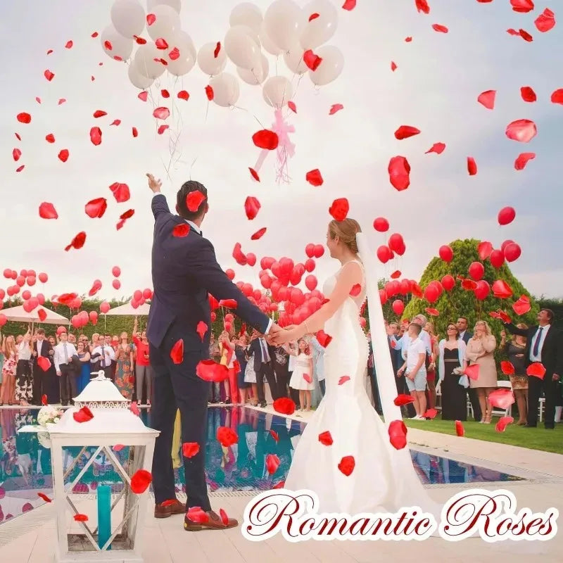 A bride and groom stand in front of a pool with red rose petals falling in the air for an event decoration.