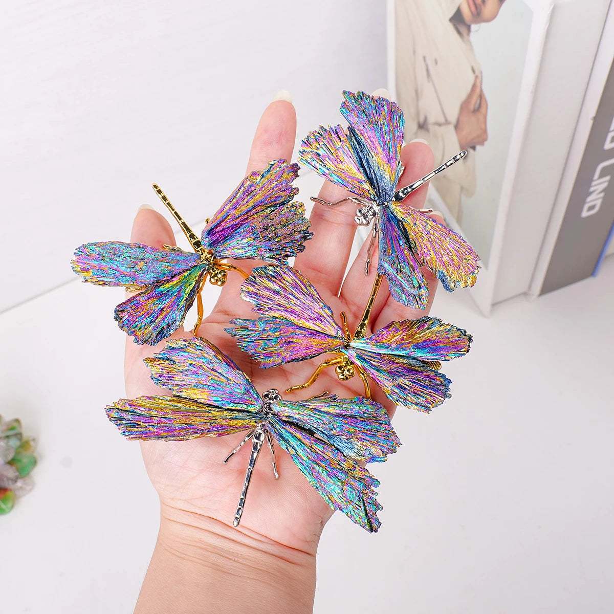 A hand holds a natural crystal tourmaline dragonfly figurine with iridescent blue and purple wings.