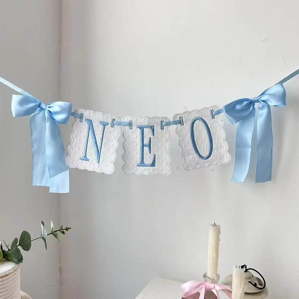 A decorative birthday garland spelling NEO made of white felt with blue ribbon bows.