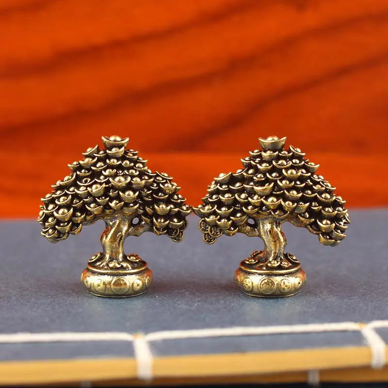 A pair of brass fortune tree ornaments with ingot accents resting on a dark surface.