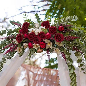 A floral arrangement of deep red roses and greenery decorating a white archway for an event.