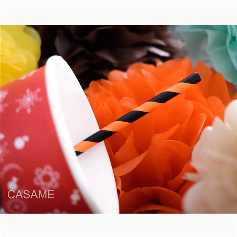 A white cup with a red polka dot design holds an orange flower, and a black and white striped paper straw is visible.