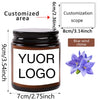 A dark glass jar candle with a white label featuring the text YOUR LOGO and a blue wind chime decoration.
