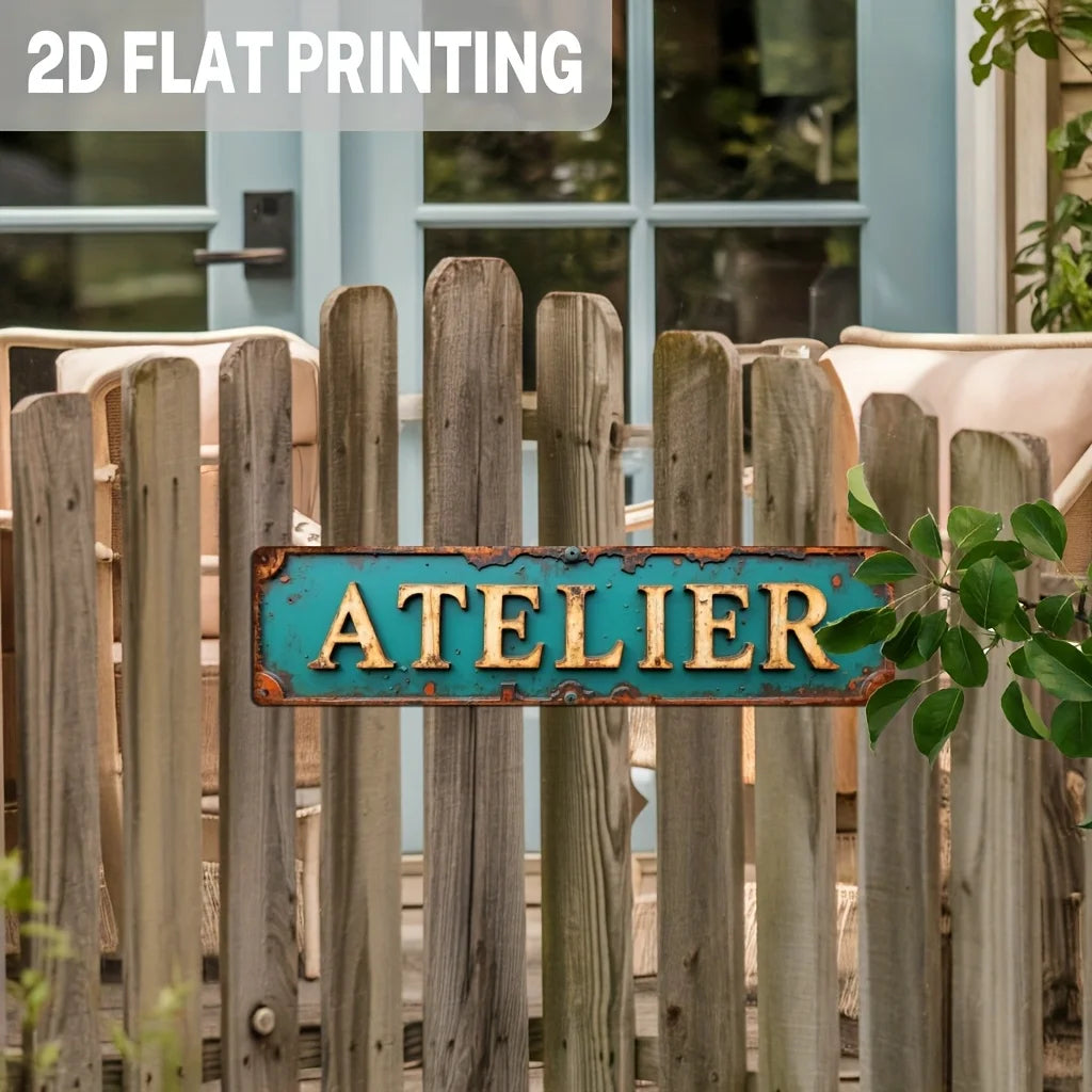 A vintage industrial metal sign with the word ATELIER in turquoise and golden distressed colors mounted on a wooden fence.